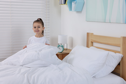 Cute girl changing bed linens in children room