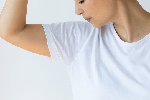 Caucasian female wearing white t-shirt is having excessive underarm sweat. Her t-shirt is wet.