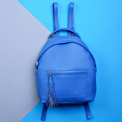 Trendy women's blue leather backpack with a top handle and a zippered pocket with a tassel pull on a two-color paper background. Creative mockup for a modern accessory store. Fashion style and trend.