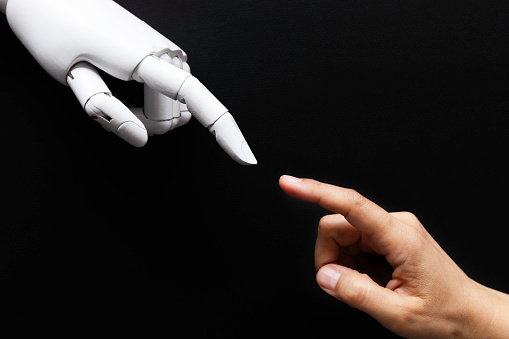Human Finger is about to touch white robot finger in front of black background.