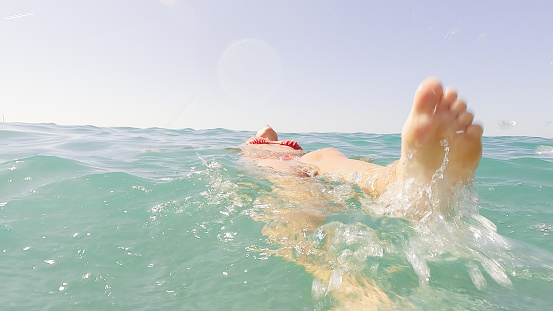 unrecognizable mature adult woman swimming on her back in the sea water and splashing with her feet in summer. concept relax, beach, vacations, wellbeing and wellness.