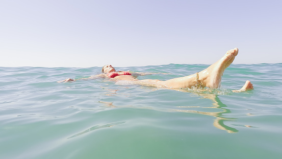 mature adult woman swimming on her back in the sea water in summer. concept of relax, wellbeing and wellness.
