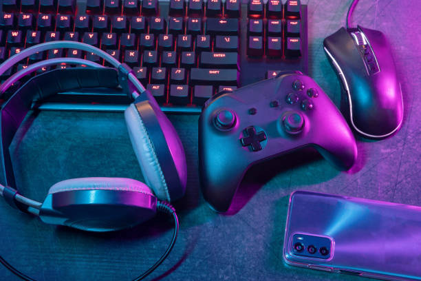 istock Top view of a gamer or streamer dynamic workspace: featuring a cutting-edge gamer keyboard, precision mouse, immersive headsets, responsive joystick, and a sleek cell phone, illuminated by neon lights 1747203607
