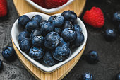 close up of blueberries in ceramic heart-shaped bowls on black.