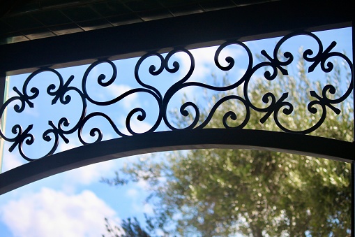 Curvy ironwork catches your eye against the background of an olive tree with clouds and blue sky