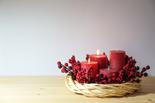 Second advent with four red candles, two of them are lit, in a natural willow wicker wreath with berry decoration, holiday home decor, copy space, selected focus, narrow depth of field