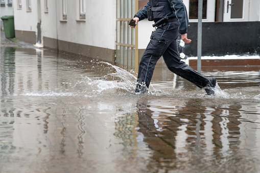 Policeman running through the water of a flooded street during high water of the river Trave in the old town of Lubeck at the Baltic sea in Germany, copy space, selected focus, motion blur