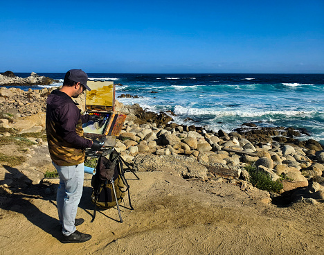 Pacific Grove, California, USA- October 11, 2023: Male plein air artist painting the scenic and rocky coastline in Pacific Grove, California.