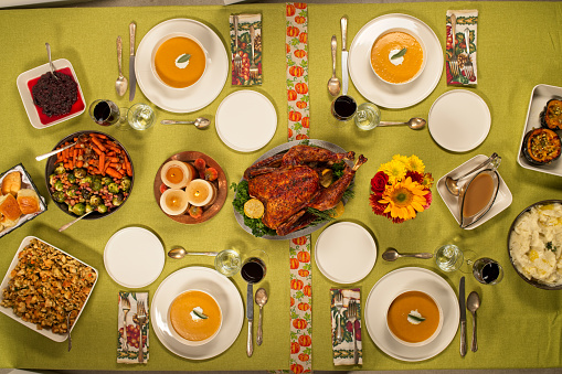 Thanksgiving dinner at a table setting with an above view of a turkey, pumpkin soup, crandberries, brussel sprouts, butter buns, gravy, stuffing