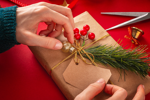 Woman preparing gift box in the center of christmas decorating items on a red background