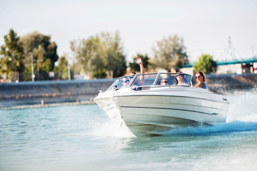 Group of young people with raised hands enjoying in a speedboat ride.