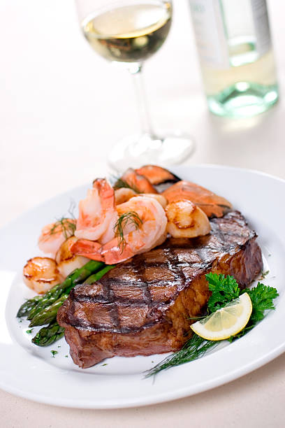 "The ultimate in surf and turf enjoyment.  A beefy portion of prime New York Strip steak complimented with a generous portion of seafood including crab legs, lobster tail, prawns and scallops.  Served with lemon and asparagus.  Shallow dof"