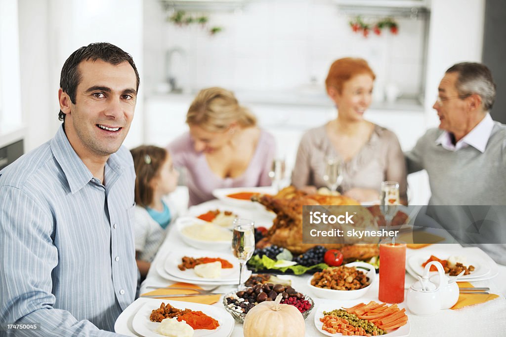 Large family at the dinner table for Thanksgiving day Happy extended family having family lunch on a Thanksgiving day.  Mid adult man looking at camera is in foreground. 30-39 Years Stock Photo