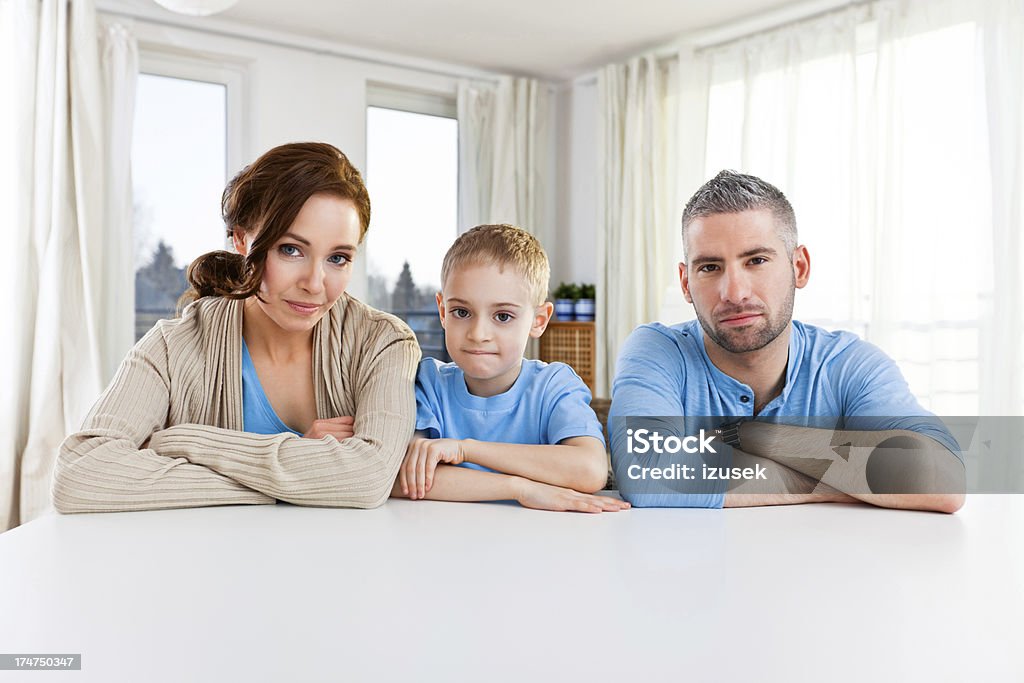 Family Portrait Portrait of young family sitting at the table with crossed arms and looking at the camera. Family Stock Photo