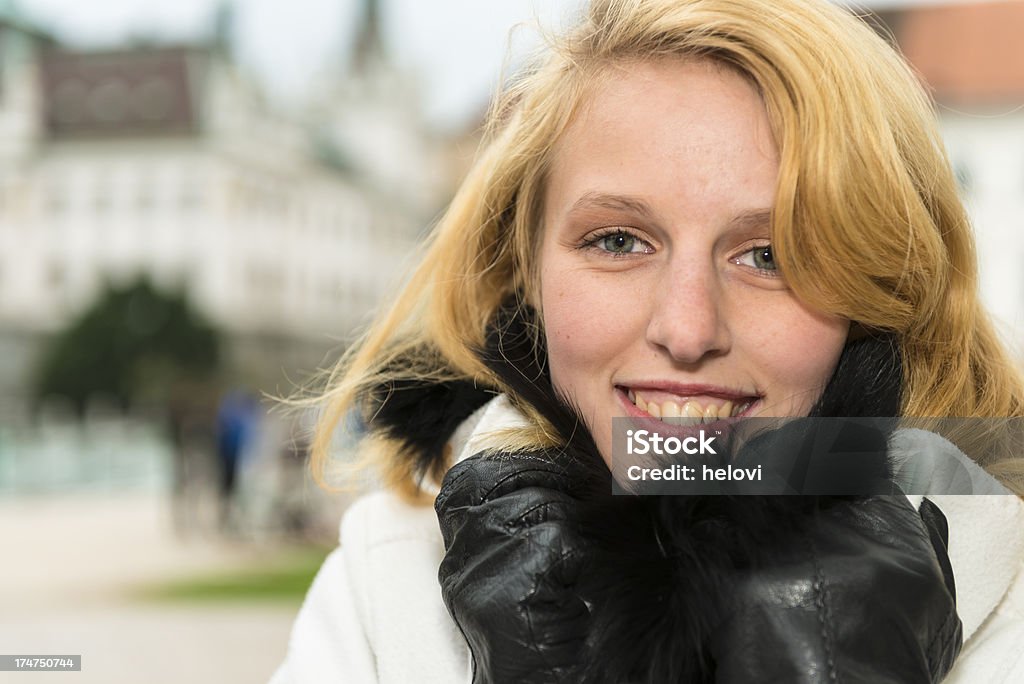 Attractive redhead "Portrait of an attractive young woman in white coat and black gloves feeling cold in fall. Urban background with blurred persons. Ljubljana, Slovenia." 20-29 Years Stock Photo