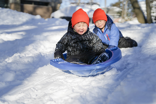 Brothers Sliding in the Snow Outdoors in Winter. They are smiling and having a lot of fun.