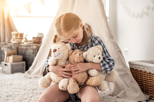 Little girl hugging plush teddy bears and in playroom