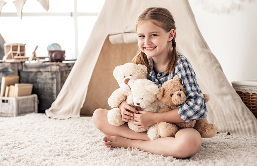 Little girl hugging plush teddies and smiling and sitting on floor in playroom