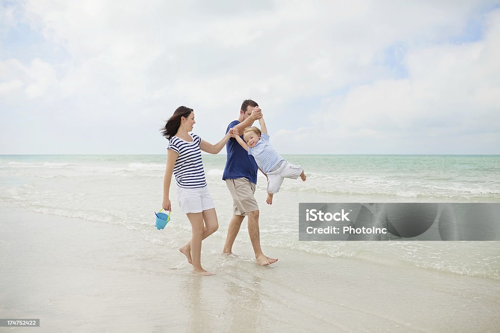 Couple heureux se balancer petit garçon dans l'Air sur la plage - Photo de 30-34 ans libre de droits
