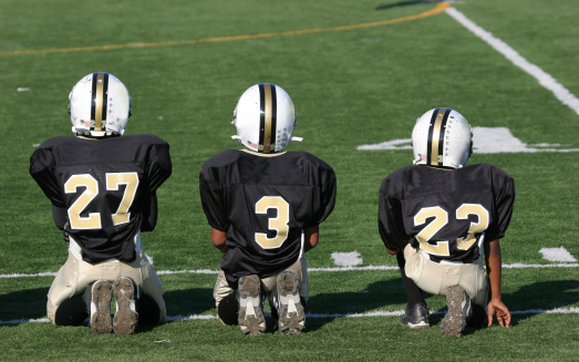 Three football players sitting on the sideline