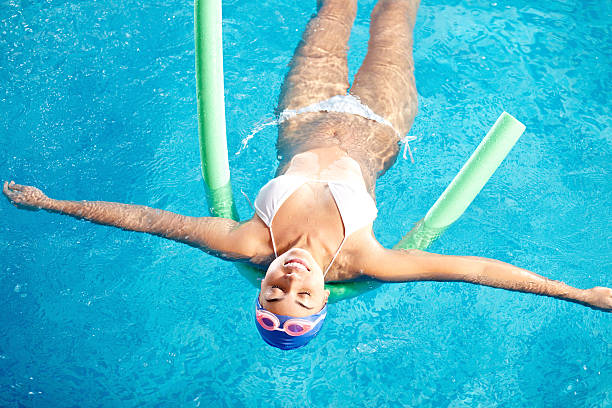 Woman relaxing in pool Happy young woman relaxing in water on sport equipment women exercising swimming pool young women stock pictures, royalty-free photos & images