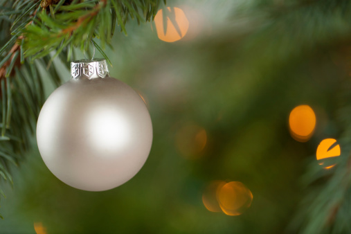 White Christmas ornaments hung from a Christmas tree with lights in the background.  Shot with copy space.