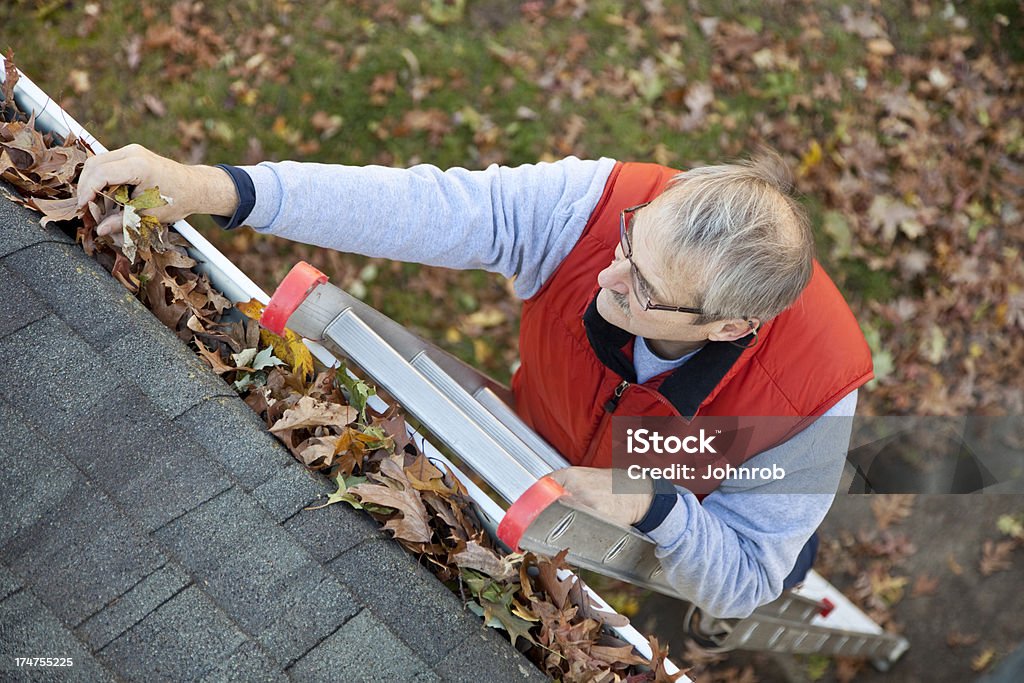 Man up ladder cleaning leafs out of gutter on house Senior man cleaning leafs out of gutter.More of this model. Cleaning Stock Photo
