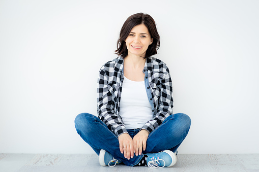 Smiling woman sitting on floor on white wall background