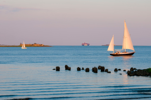 Two sailboats going opposite directions on an early summer evening in Charleston Harbor in South Carolina. In the far distance is a cargo ship and the Fort Sumter ferry. Fort Sumter is behind the sailboat on the right.