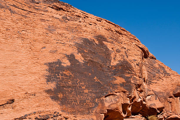 Ancient Petroglyphs on the Canyon Wall Valley of Fire is Nevada’s oldest state park. The park gets its name from the red rock formations which appear to be on fire as the sun sets. These Aztec sandstone rocks were formed from sand dunes 150 million years ago. The region was further shaped by uplifting and faulting followed by extensive erosion. The Anasazi people visited this area from about 300 BC to 1150 AD. Scarcity of water would have prevented their living here but they probably hunted, gathered food and performed religious ceremonies. There are several sites where their petroglyphs can still be seen. In 1931, 8,760 acres of federal land was transferred to the state of Nevada. In 1933, the Civilian Conservation Corps (CCC) began developing the park which opened in 1934. The CCC continued working on the park into the early 1940’s and built campgrounds, trails, visitor cabins, ramadas and roads. In 1935, the Nevada State Legislature designated the area as Valley of Fire State Park. In 1968, the park was recognized as a National Natural Landmark. This scene of ancient petroglyphs was photographed at Petroglyph Canyon. Valley of Fire State Park is located 50 miles northeast of Las Vegas near Overton, Nevada, USA. jeff goulden valley of fire state park stock pictures, royalty-free photos & images