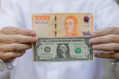 Primer plano de las manos de un hombre sosteniendo un billete de un dólar junto a un billete de mil pesos argentinos. photo
