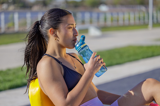 Latin girl in sportswear drinking water on an outdoor exercise machine.