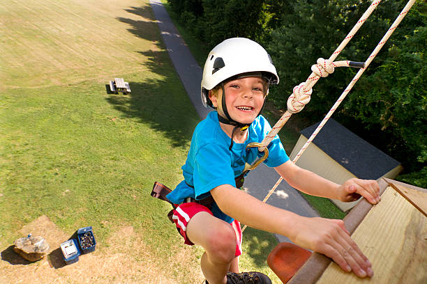 Seen here is a six year old boy climbing on a tall outdoor climbing tower / rock wall.  Wide view from above.