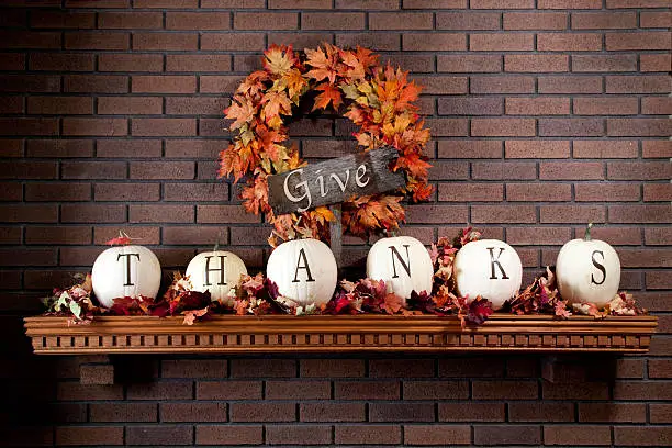 Pumpkin painted with the words give thanks resting on fireplace mantel with colorful Fall leaves.