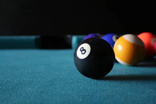 Eight ball in the foreground on pool table with pocket and black background.  Plenty of room for text.