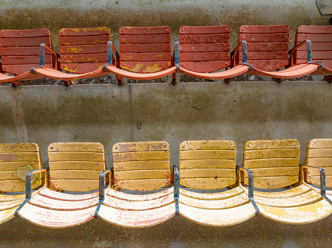 Old faded orange and yellow painted wooden seats at a abandoned a stadium grandstand.
