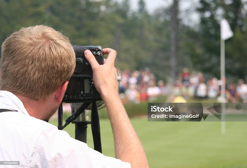 Sports Journalist Photographing Professional Golf Tournament A professional sports journalist shooting a golf event. Sports journalism is a popular vocation for sports fans. Here a professional photographer captures an image of a pro golfer shooting out of a sand trap. Models are unrecognizable and golf tournament is a professional event. Photographer is male Caucasian in his 30s.  Golf Stock Photo