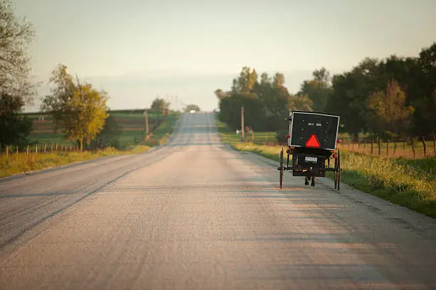 An Amish horse and buggy slowly make their way down a deserted road at sunrise.