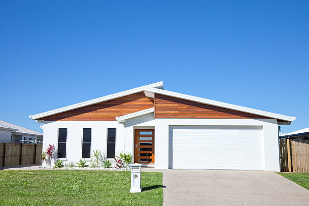 Front view of a new neat modern white low set single story family home with green grass and blue sky for copy space.