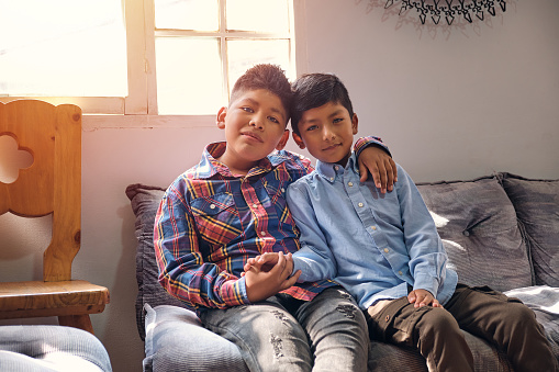 two brown-skinned Latino brother and sister children happily hugging in a room