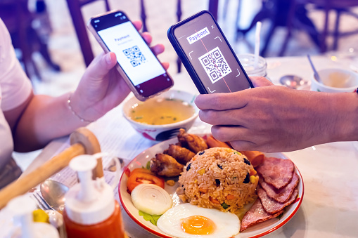 Hand using smart phone to scan simulate QR code on tag with blurry Thai food in cafe or restaurant to accepted generate digital pay without money. Qr code payment concept.