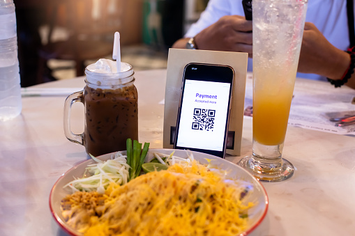 Simulate Qr Code tag on smartphone with blurry Thai food in cafe or restaurant to accepted generate digital pay without money. Qr code payment concept.