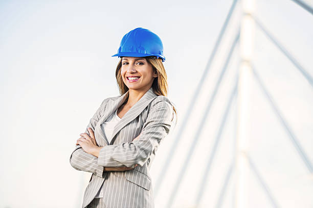 Cheerful female architect wearing a hardhat is looking at camera. Bridge is in the background.
