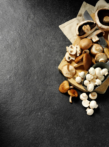 A mixture on edible mushrooms on a wooden chopping board with a antique knife on a dark slate background.Click on the link below to see more of my fruit and vegetable images