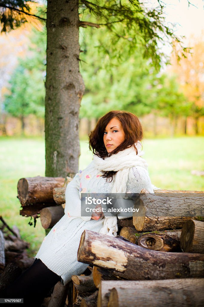 Attractive young woman leaning on pile of logs in park "Attractive young woman dressed in warm and cosy white sweater is leaning on pile of logs and folding arms in autumn park.If you download this image, please let me know how you want to use it. This information is for my private use only. Thank you." Adult Stock Photo