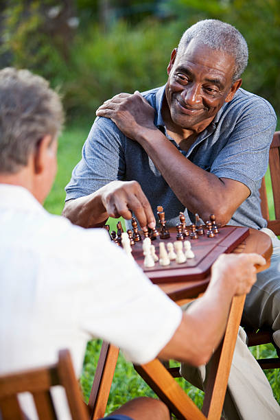 Senior men playing chess in park Multi-ethnic senior men (60s) playing chess outdoors.  Focus on African American man. senior chess stock pictures, royalty-free photos & images