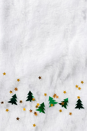 Merry Christmas and Happy New Year background with sparkling golden stars sequins and fir tree shape green color confetti on white fur, copy space. Minimal top view, winter holidays greeting cards