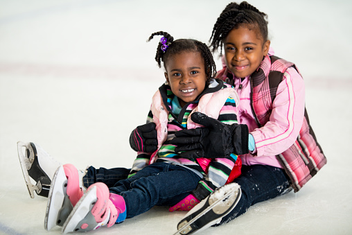 Sisters sitting on ice with skates.