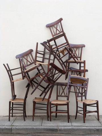 A stack of wooden chairs up against a white painted wall.