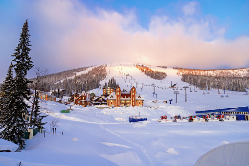 Sheregesh ski resort in Russia, picturesque sunrise, pink cloud on sky, white snow slopes and trails, view on mountain Green (mount Zelenaya), hotels, lift stations, Russia, Siberia. Panoramic view